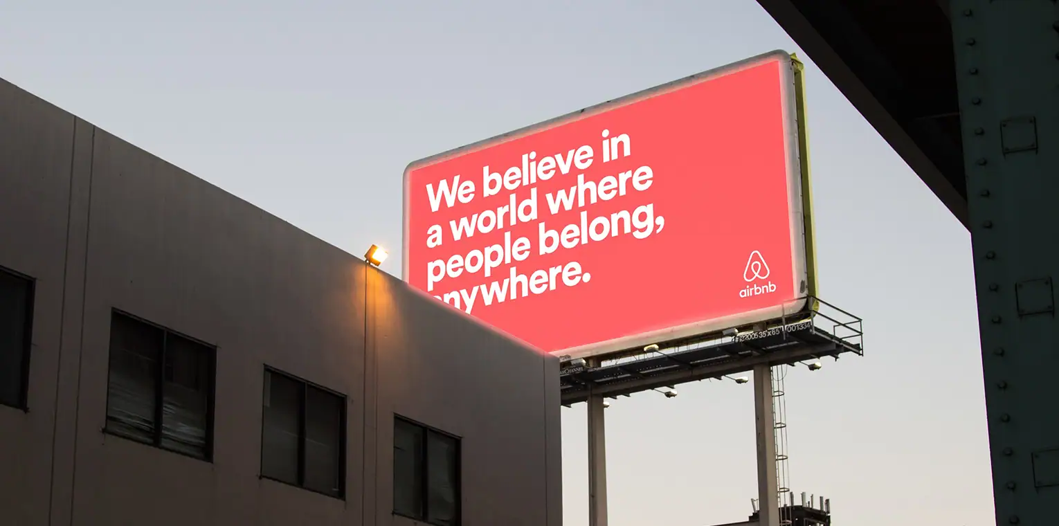 Panou publicitar Airbnb cu mesajul „We believe in a world where people belong, anywhere" — exemplu de identitate vizuală aplicată consistent în comunicarea outdoor